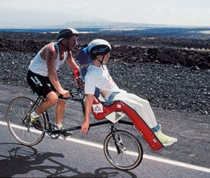 After carrying his son sometimes more than a quarter mile from the water to a changing station, the two set out on a specially-designed bike for 100+ mile jaunts through volcano fields. Dick pedals the bike, which can be in excess of 400 pounds at times, up craters and across vistas in heat that can exceed 110 degrees.